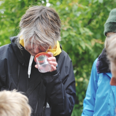 Person schaut in ein Becher und andere Menschen schauen zu